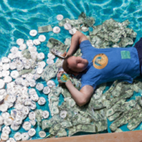 a man lies carefree in a swimming pool full of dollar bills and coins